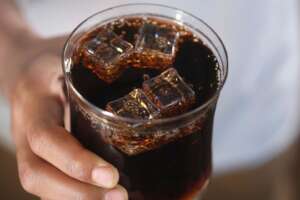 Mano sosteniendo un vaso de refresco de cola con hielo