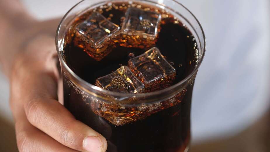 Mano sosteniendo un vaso de refresco de cola con hielo